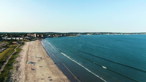 beachgoers sunbathe and calm waves lap the shoreline at nahant beach, aerial