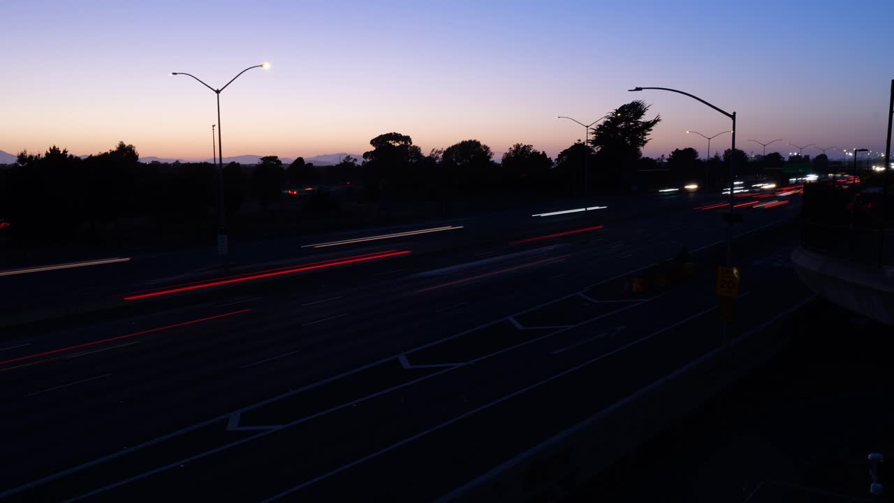 Vehicles stream steadily along I-80 in Berkeley, their lights forming continuous ribbons of motion under fading daylight.