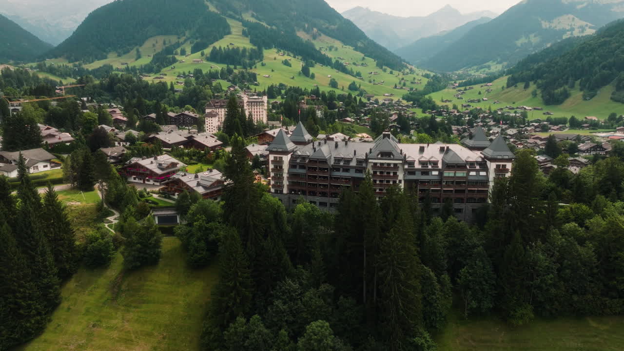 Gstaad Palace hotel surrounded by a lush forest, aerial orbit view