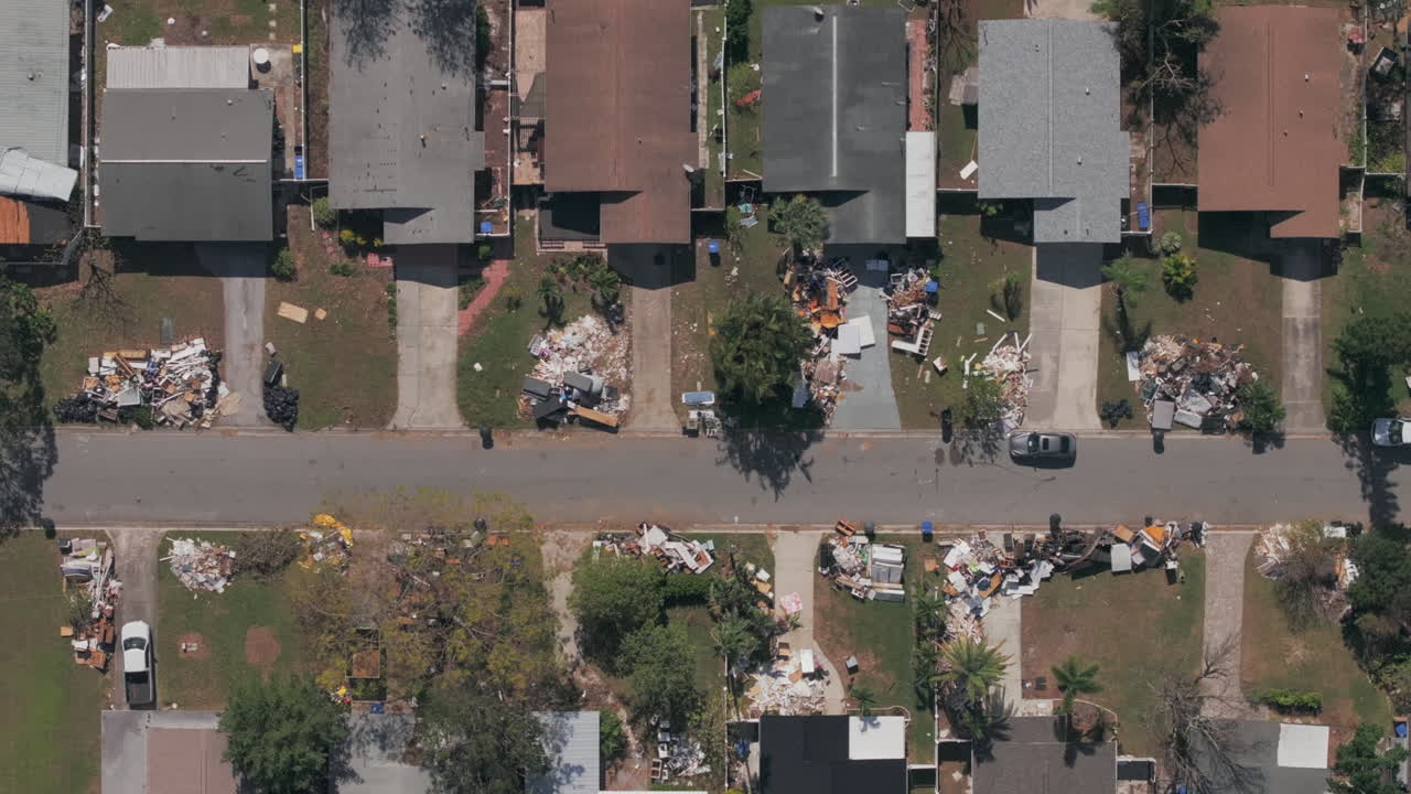 Aerial top-down shot shows rows of houses in St. Petersburg Florida neighborhood with varying degrees of destruction, from piles of trash and debris to roof damage in the wake of Hurricane Milton.