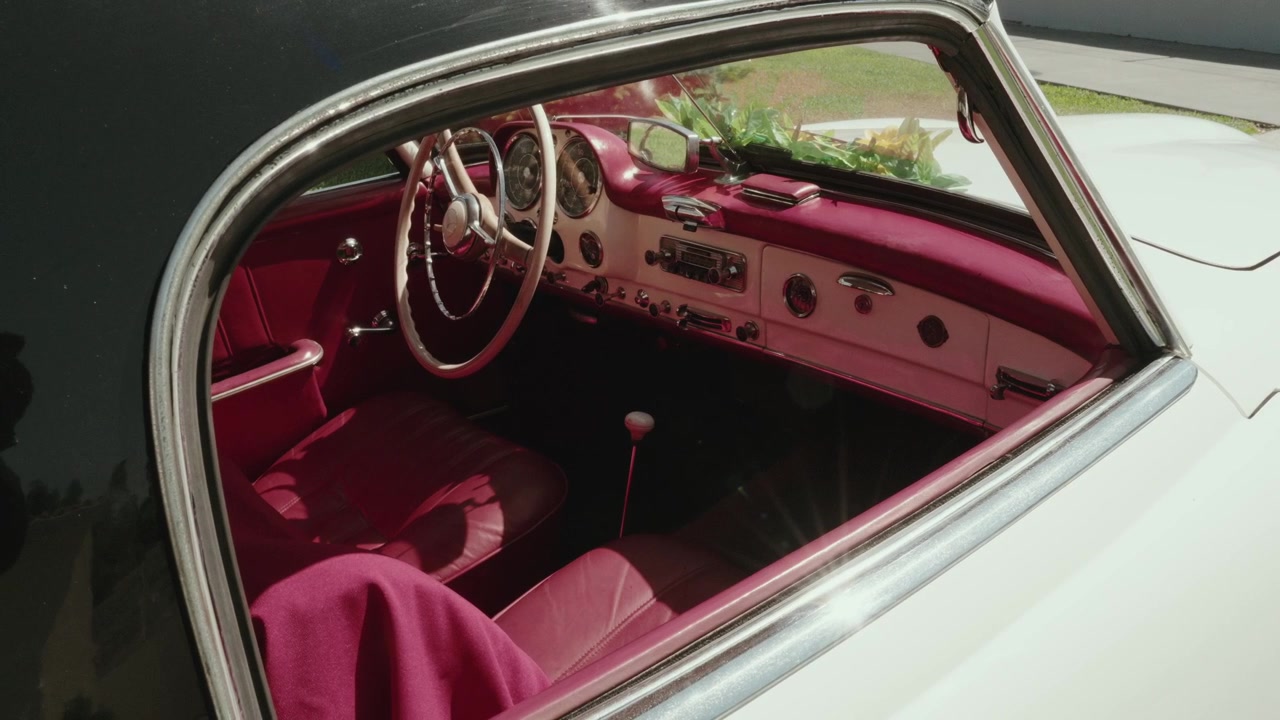 Sisäkuva klassisesta vintage-autosta, näyttäen punaisia nahkaistuimia, kojelautaa ja ohjauspyörää