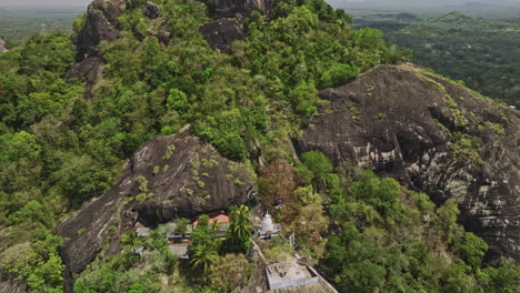 Algama-Len-Viharaya-Sri-Lanka-Aerial-v2-birds-eye-view-fly-around-ancient-hillside-cave-Buddhist-temple,-tilt-up-reveals-jungle-rock-and-mountain-landscape-views---Shot-with-Mavic-3-Cine---April-2023