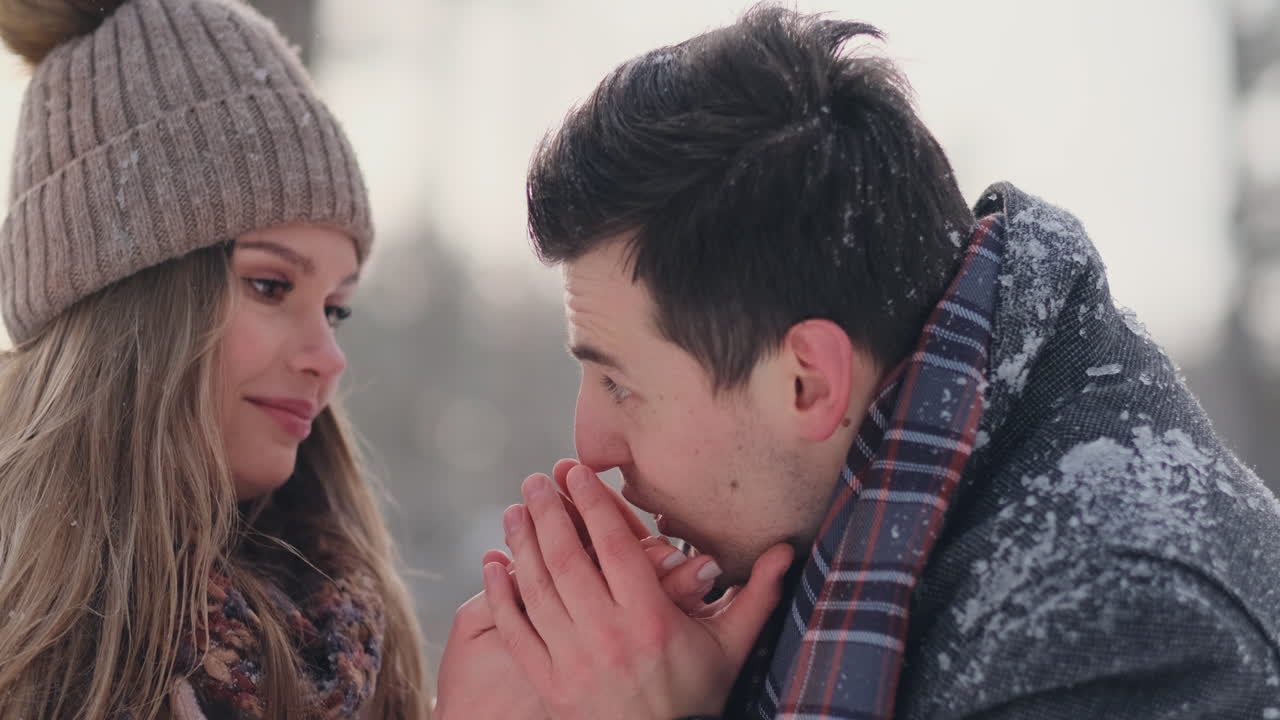 A caring man warms his wife's hands in the winter on the street in a snow-covered Park.
