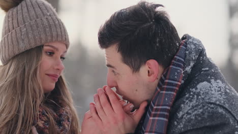 a caring man warms his wife's hands in the winter on the street in a snow-covered park.