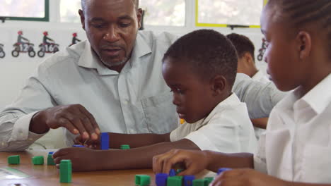 Teacher-helping-elementary-school-boy-counting-with-blocks