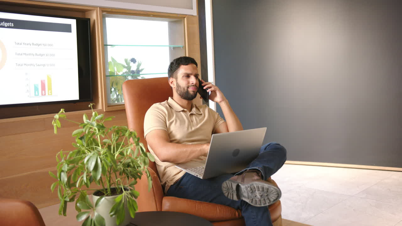 Working from home, man using laptop and talking on smartphone in office