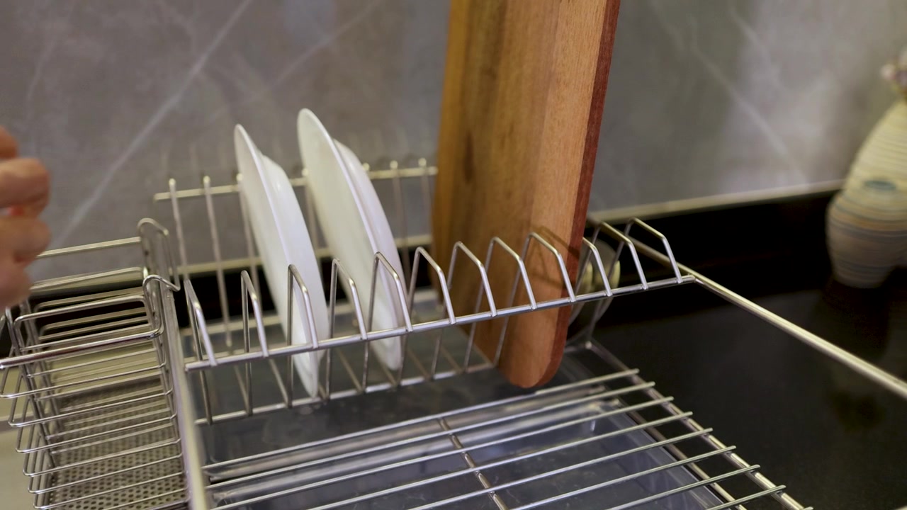 A person places clean white ceramic plates into a stainless steel drying rack neatly.