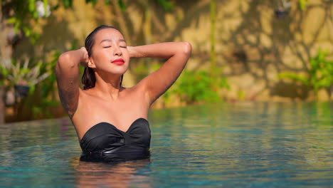 a beautiful woman emerges from a swimming pool brushing her wet hair away from her face