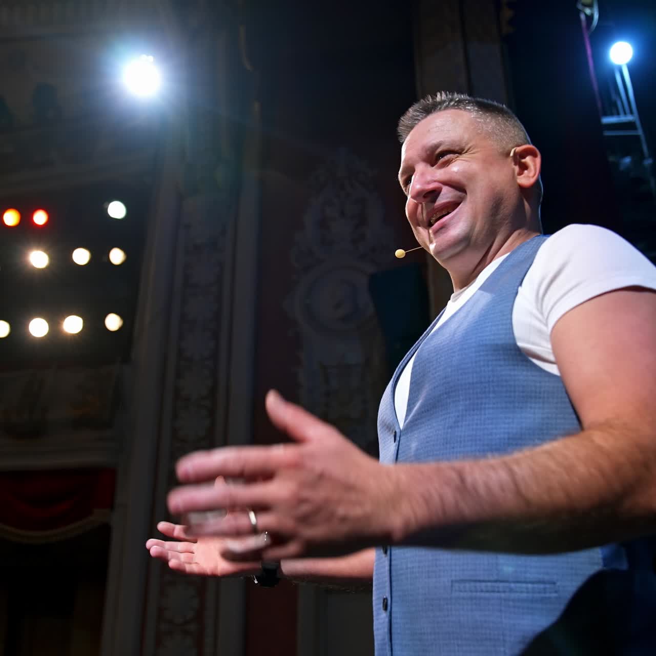 Smiling actor on stage. Middle-aged man standing on the scene of a theater and talking to the audience. Acting at bright spotlights. Side view