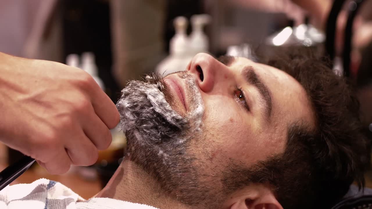 Mand, der får sit skæg barberet med en ragekniv i en barberforretning