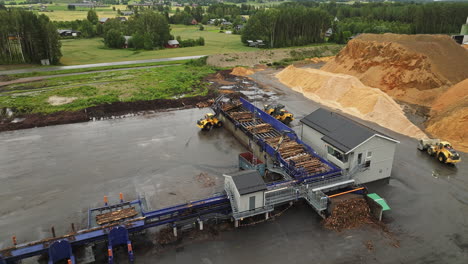 conveyor system moves logs next to piles of sawdust at lumber yard, aerial