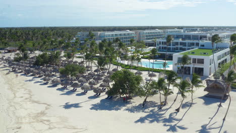 Exotic-palm-beach-with-parasols-in-front-of-luxurious-hotel-resort