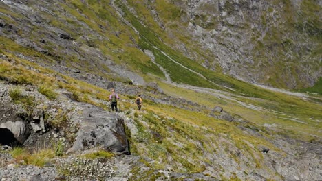 panorámica de una pareja de excursionistas haciendo senderismo cuesta abajo por montañas verdes empinadas durante un día soleado en gertrude saddle