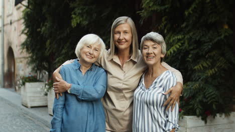 Retrato-De-Tres-Lindas-Mejores-Amigas-Paradas-En-La-Calle-De-La-Ciudad,-Abrazándose-Y-Sonriendo-A-La-Cámara