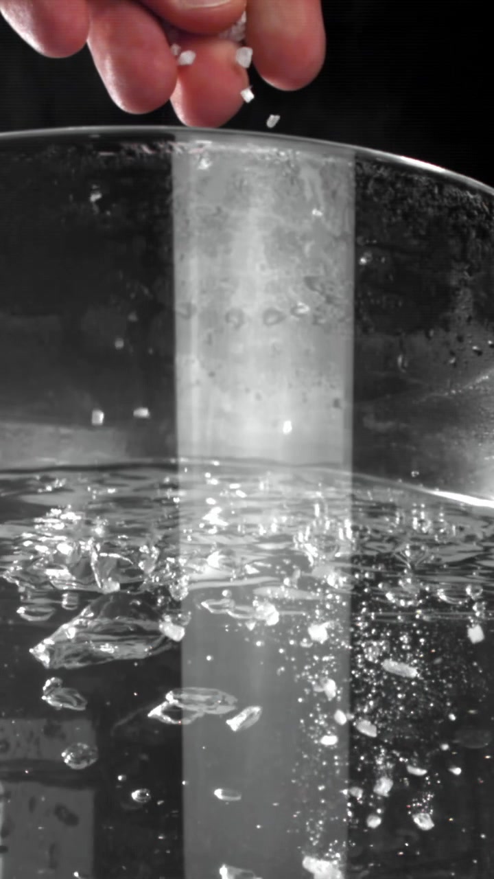 Mano che lascia cadere cristalli di sale in acqua limpida al rallentatore