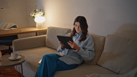 focused model watching tab at lamp light place. calm woman looking tablet screen