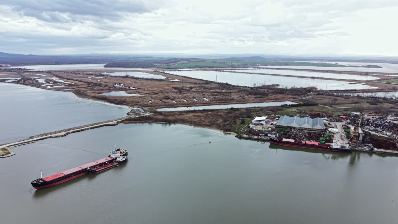 Cargo ship sails near coastal area with water and land surrounding it on a cloudy day in a port region