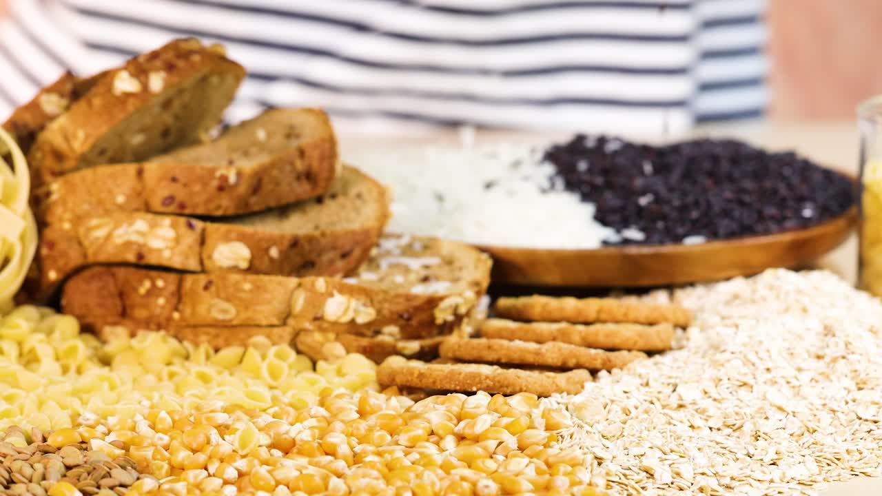 Hands organize various grains and breads on a table, showcasing a colorful assortment of food items in bright lighting