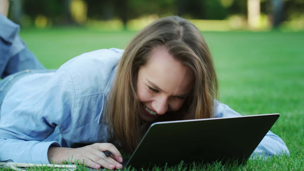 Happy woman laughing while using laptop computer on green lawn in summer park