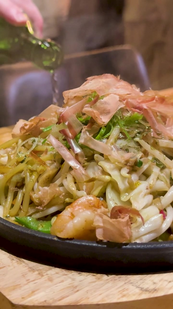Versare la salsa su yakisoba giapponesi fumanti con gamberetti e scaglie di bonito