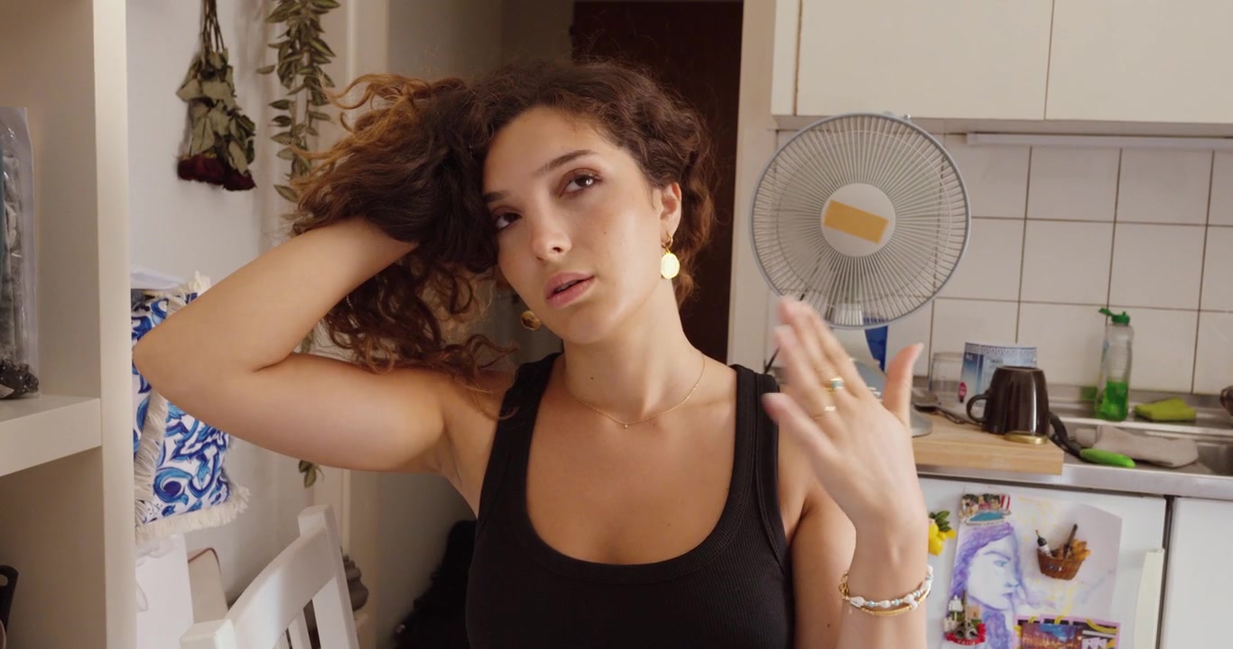 Una donna si rinfresca con la mano mentre si sente accaldata al chiuso con un ventilatore elettrico in funzione sullo sfondo