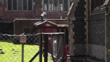 Steamy-gas-escaping-a-chimney-on-a-sunny-day-behind-a-church-in-London,-England