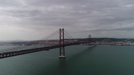 Aerial-view-to-Bridge-Ponte-25-de-Abril-over-the-Tagus-river-in-Lisbon,-Portugal-on-a-sunny-day-with-fluffy-clouds