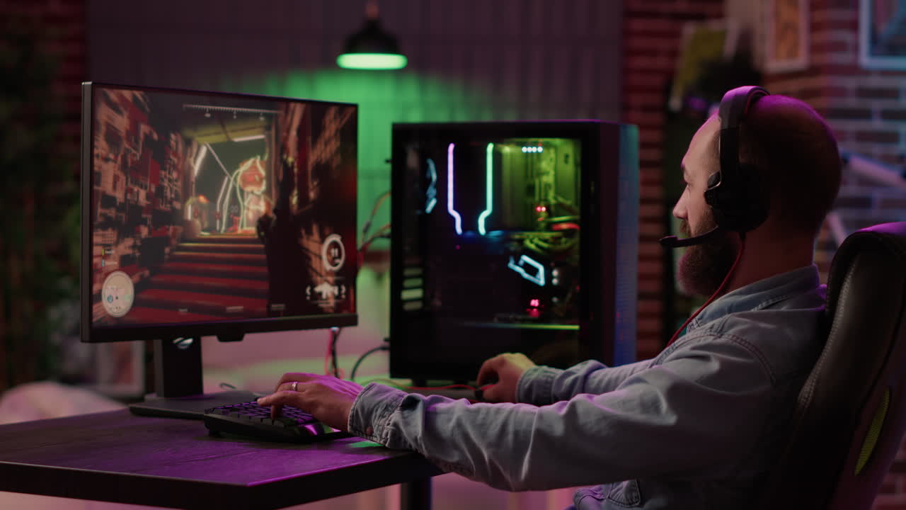 Static tripod shot of man using pc setup playing multiplayer online action game talking to team