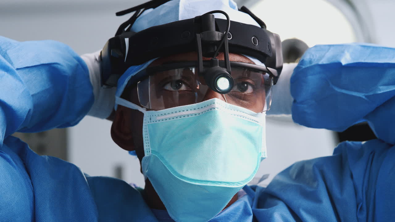 Male Surgeon With Protective Glasses And Head Light Putting On Mask In Hospital Operating Theater