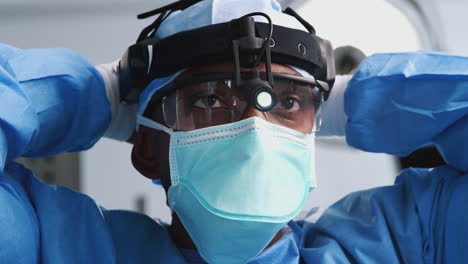 male surgeon with protective glasses and head light putting on mask in hospital operating theater