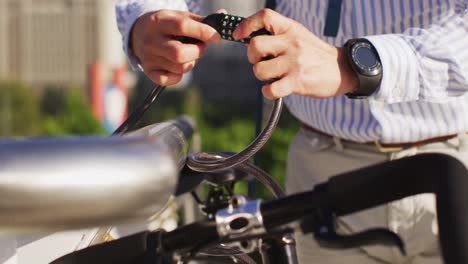sección media de hombre asiático bloqueando su bicicleta en el parque corporativo