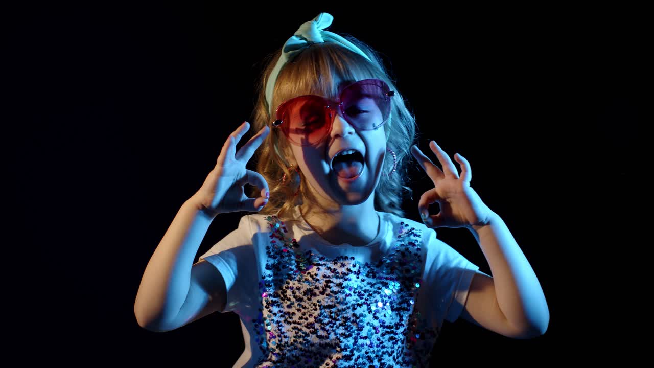 retrato de una joven rubia en brillantes rayos de neón de colores que muestran una señal de ok en un fondo negro
