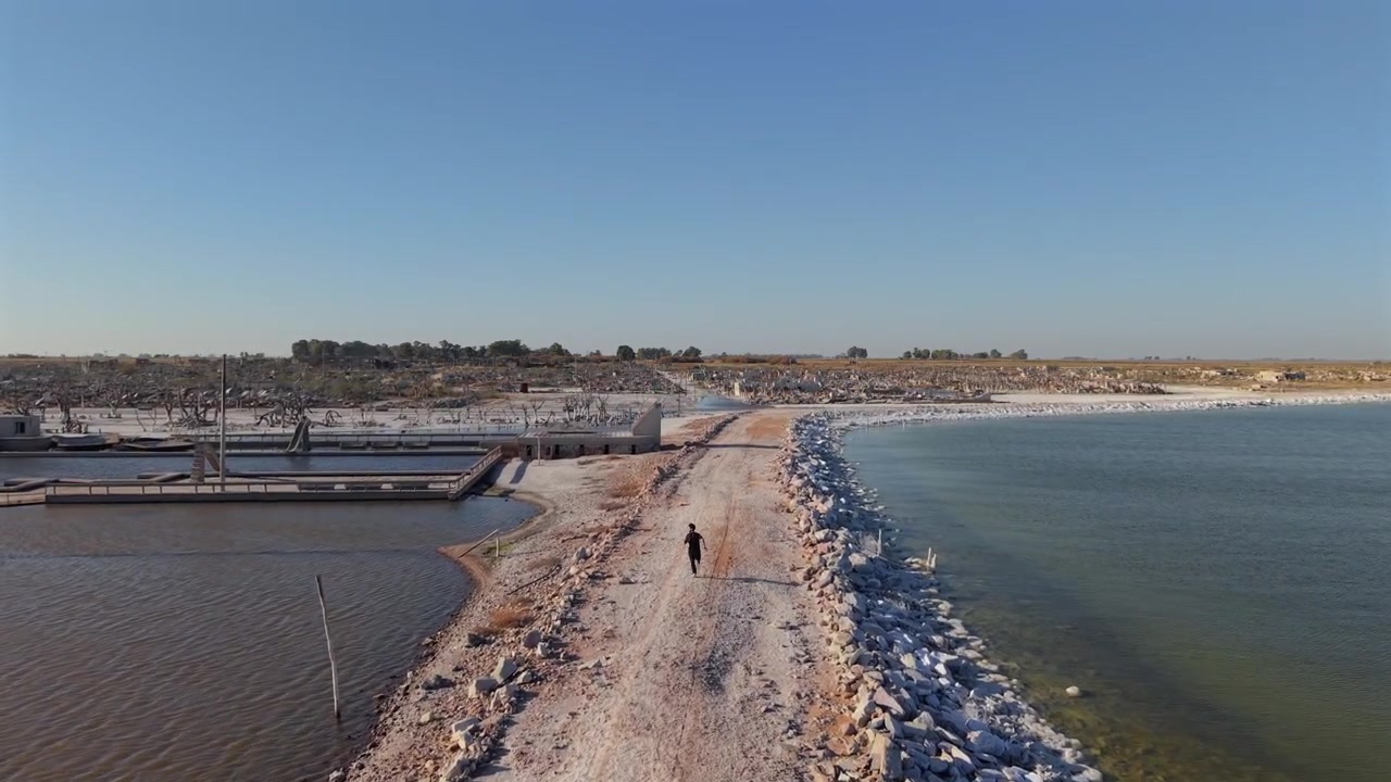 Carrellata con drone di un uomo che corre verso le rovine di una città abbandonata a Villa Epecuén, Argentina