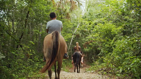 slow motion back shot of group in line horseback riding on in tropical forest pathway in cancun, mexico