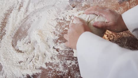 Asian-female-baker-working-in-bakery-kitchen,-kneading-dough-on-counter-in-slow-motion