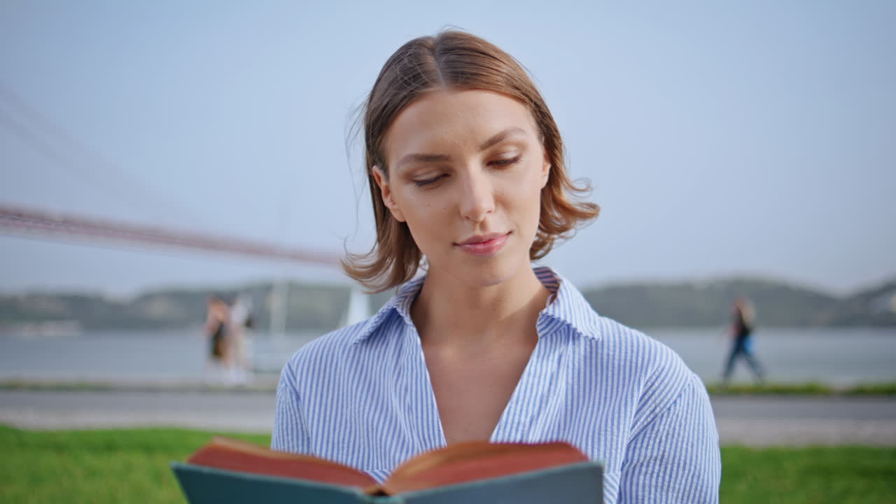 Woman reading novel nature sitting in front river bridge closeup. Serious lady