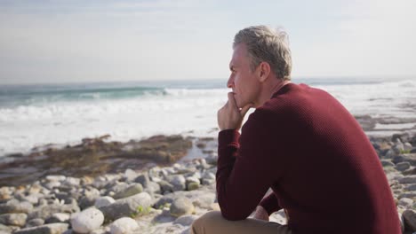 Caucasian-man-enjoying-free-time-by-sea-on-sunny-day-sitting-and-thinking