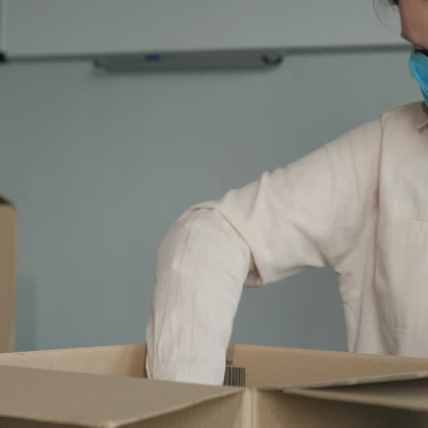 a woman in a mask and gloves packs food into cardboard shipping boxes