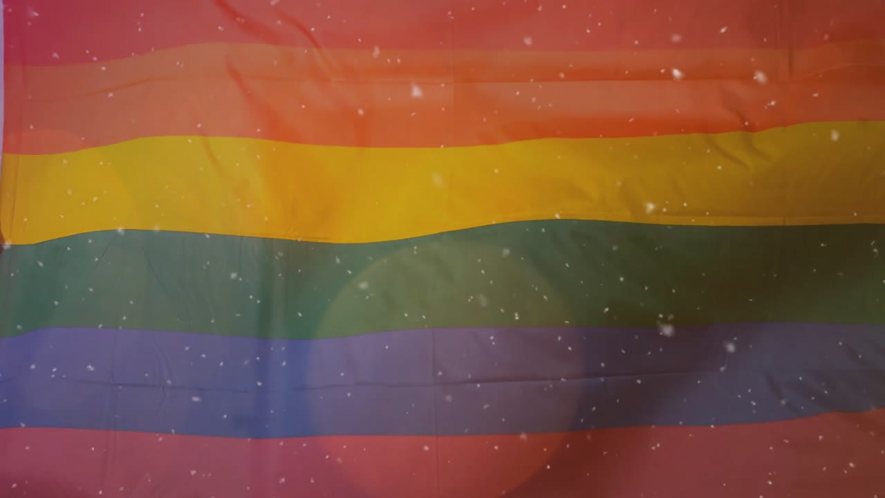 Rainbow pride flag fabric unfolding in close-up view, showing confetti flecks and lens-flare glow