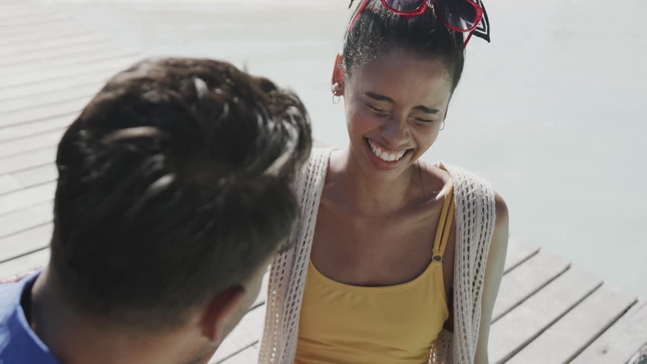 una pareja feliz hablando y riendo sentada junto a la piscina en la terraza, en cámara lenta.