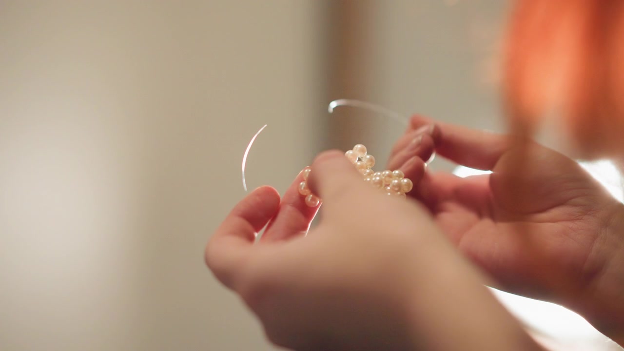 Mani con pendolo. Pendolo di cristallo su superficie perlinata. Primo piano di mani che tengono un pendolo di cristallo sopra delle perline. Scena intima di mani che guidano un pendolo di cristallo su una superficie perlinata.