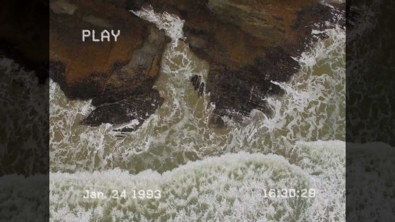 Ozeanwellen branden gegen Felsen, ausgelöst durch die steigende Flut, und zeigen den Wellenschlag mit einem VCR-Overlay.