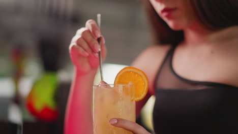 woman stirs cocktail with straw in bar closeup. young lady with delicious exotic alcoholic drink rests in club. party guest enjoys beverage