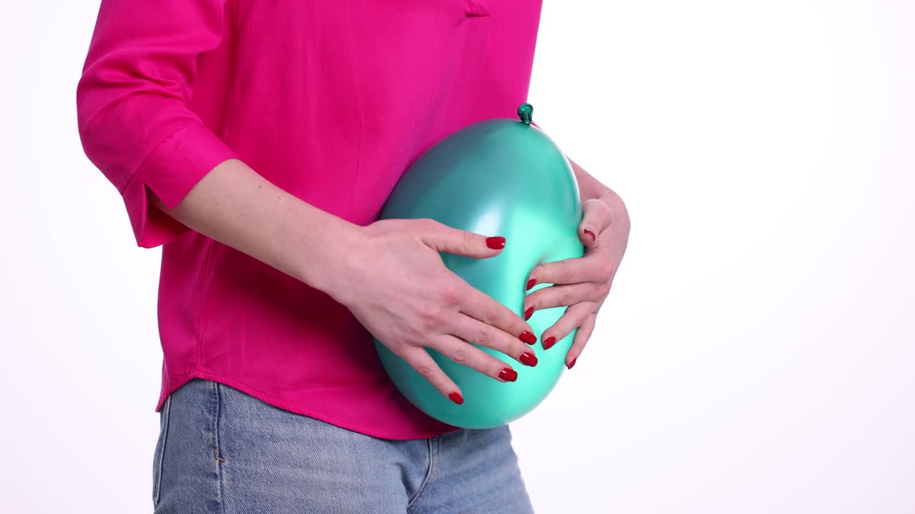 Persona che tiene un palloncino color verde acqua contro lo stomaco, simulando una pancia gonfia.