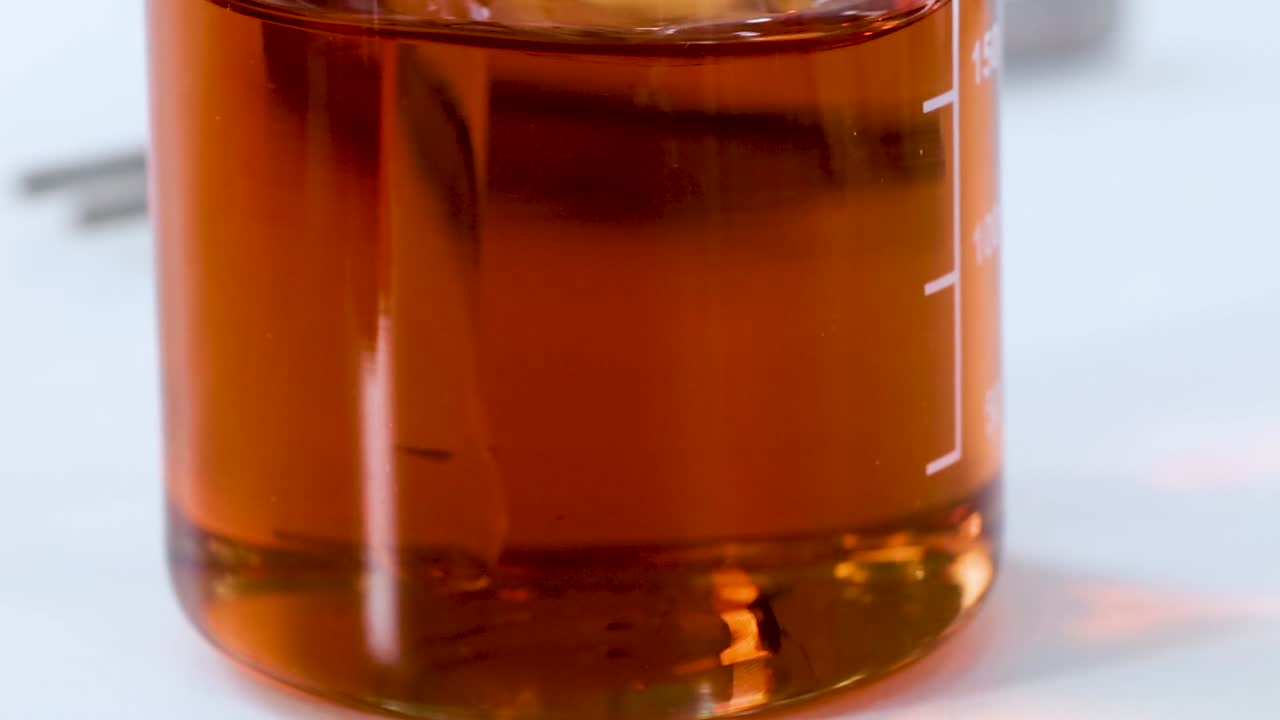 Close-up of an orange liquid in a beaker being stirred with a rod.