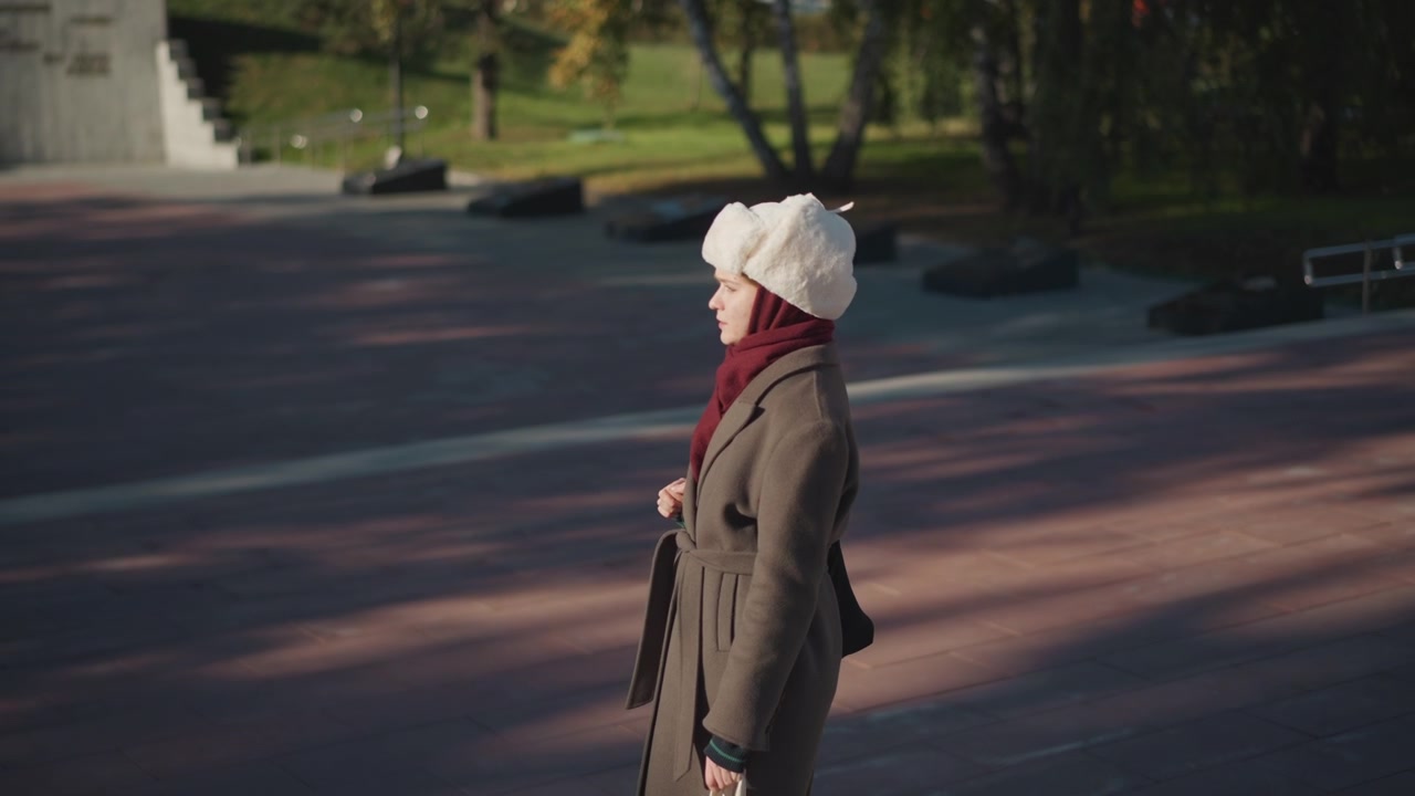 Giovane donna con cappotto invernale e cappello di pelliccia in piedi nel parco