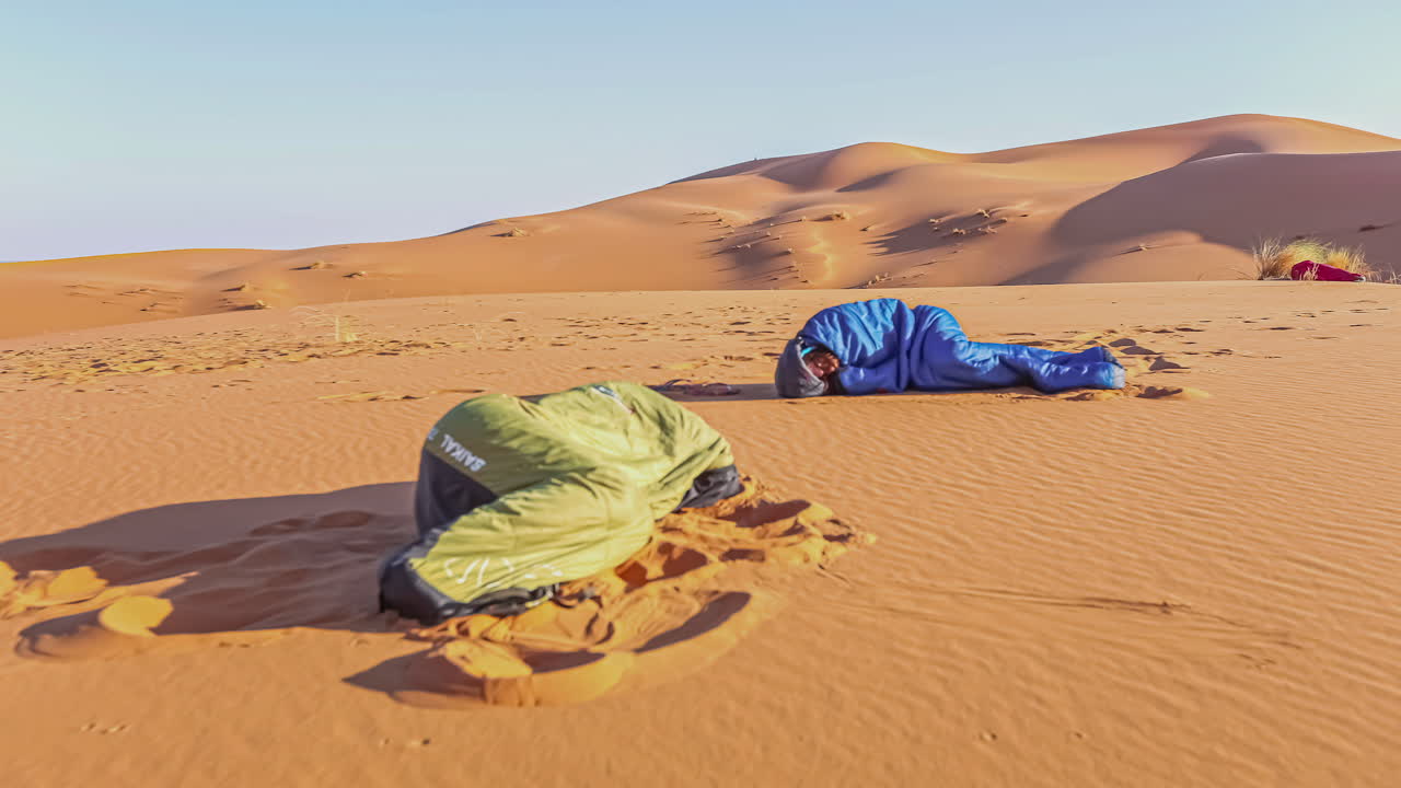 Two people camping and in sleeping bags as the sun rises in Morocco's Sahara Desert - time lapse