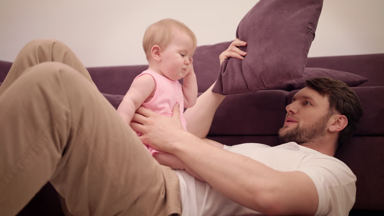 Dad playing with baby on sofa. Father time. Joyful dad and daughter