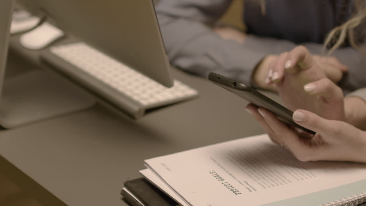 крупный план двух неузнаваемых сотрудниц, что-то рассматривающих в мобильном телефоне в офисе