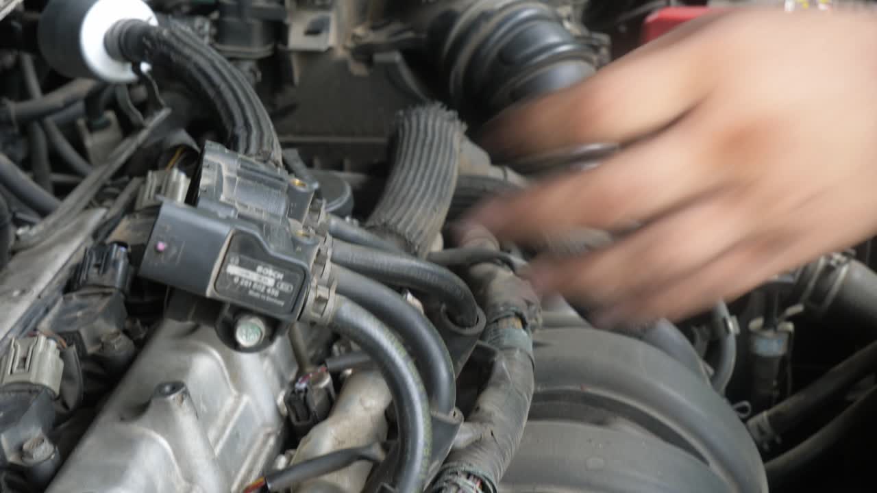 A close-up shot of a mechanic's hands while working on the engine of a vehicle in a repair shop in Bangkok, Thailand